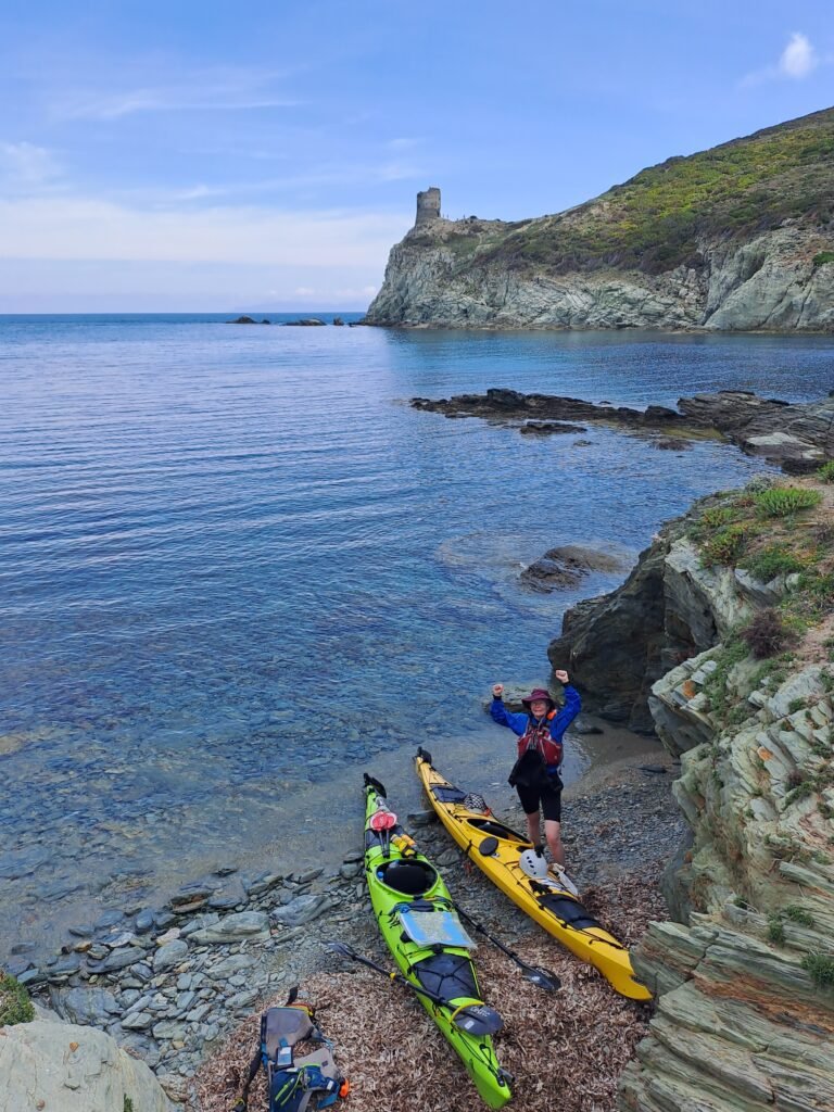 Tina standing in front of the kayaks with a Genoese tower in the background